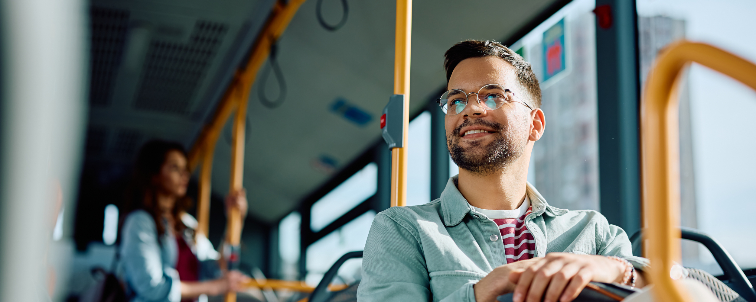 Ein junger Mann mit Brile sitzt glücklich in einem Bus