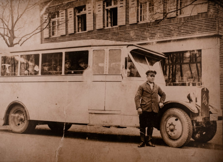 1935 Ein Mann posiert vor einem altertümlichen Bus, der bereits Gäste eingeladen hat